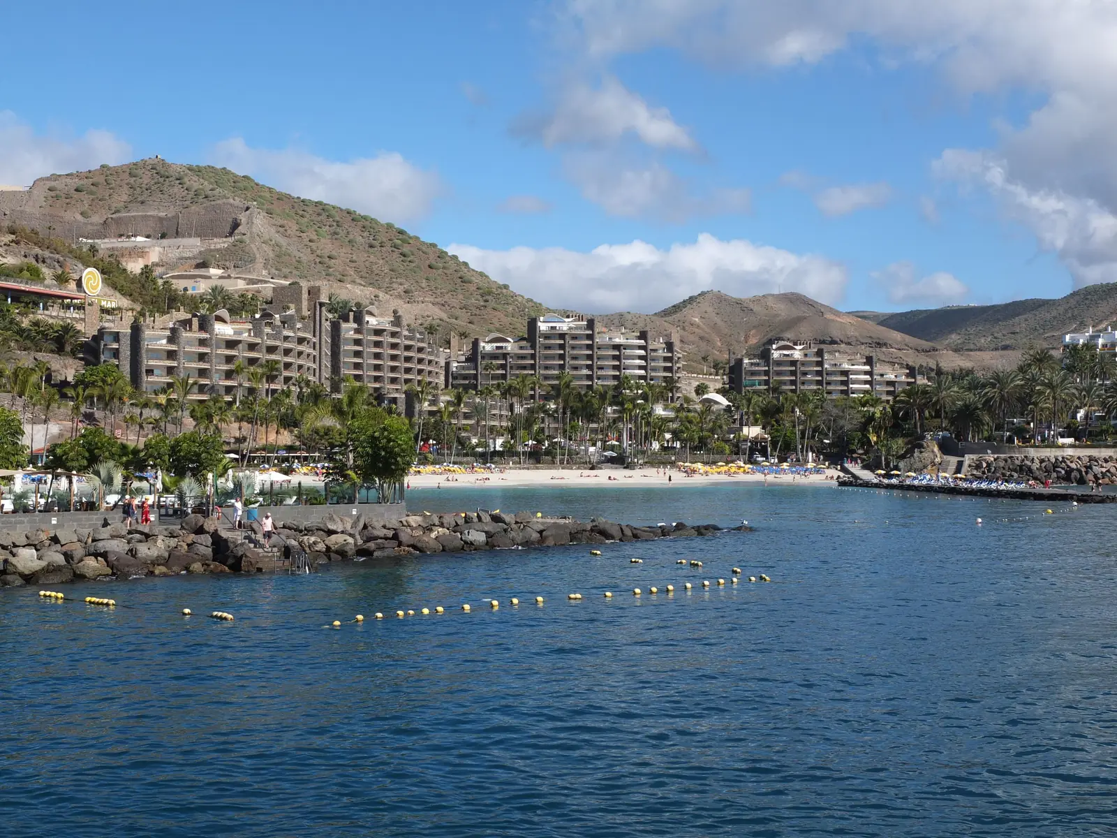 Anfi Beach seen from the pier, with the beach, palm-fringed hotels and brown hills behind