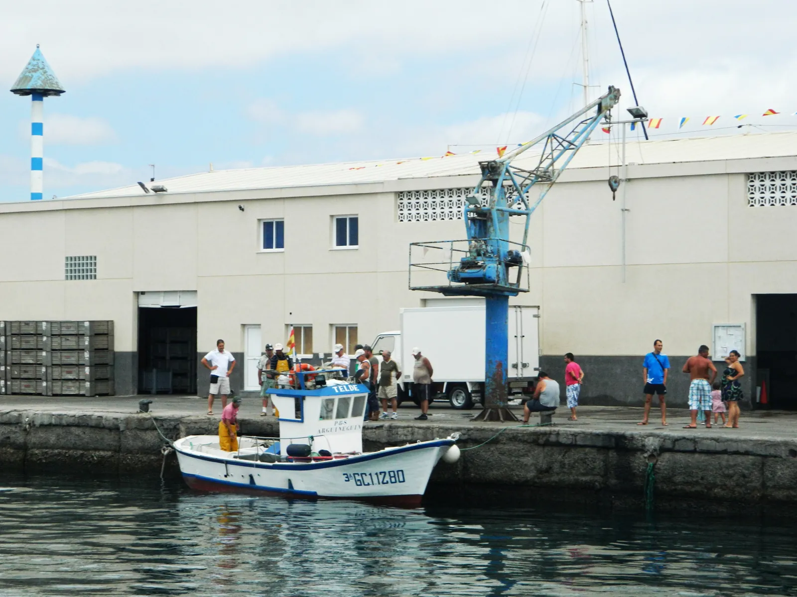 Fishing boat moored at the quay of Arguineguín harbour beside a blue crane and the fish market building