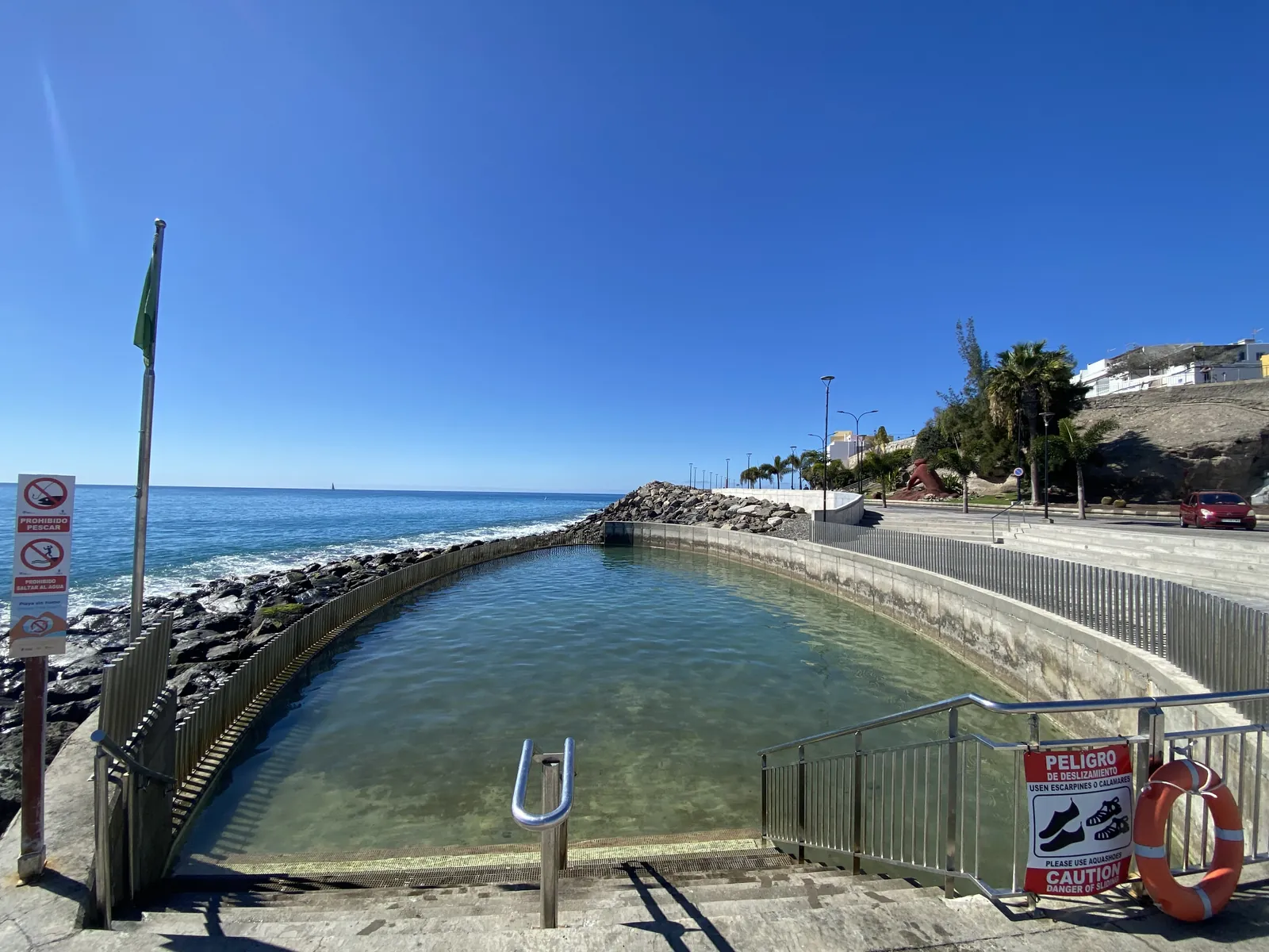 Tidal swimming pool on the Arguineguín seafront with the Atlantic and a green flag under a deep blue sky