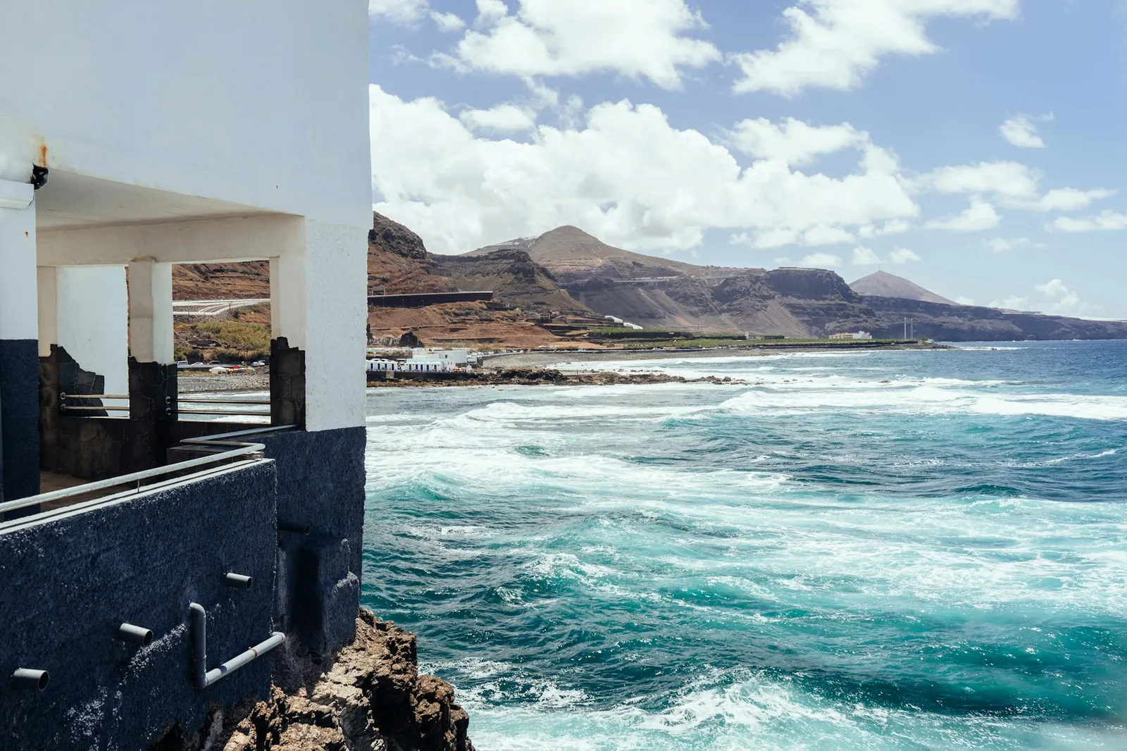 Turquoise surf breaking along a rocky Gran Canaria shore beside a white seafront building