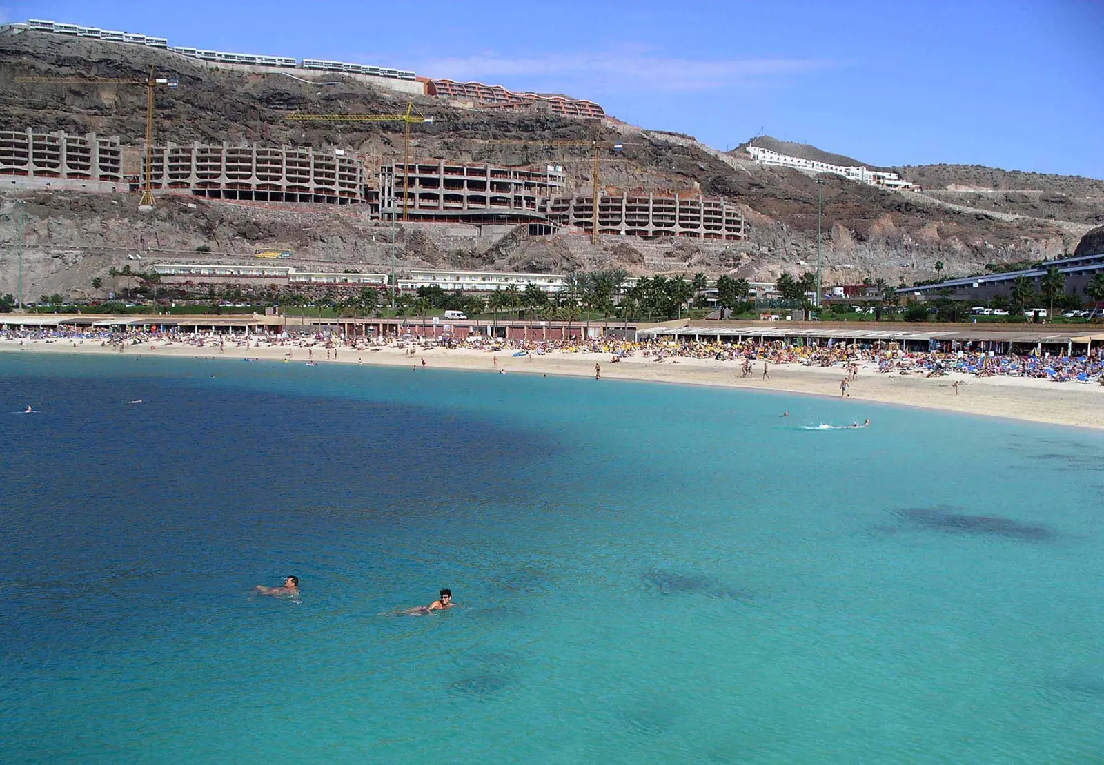 Swimmers in calm turquoise water off a sandy beach with sunbathers on the shore