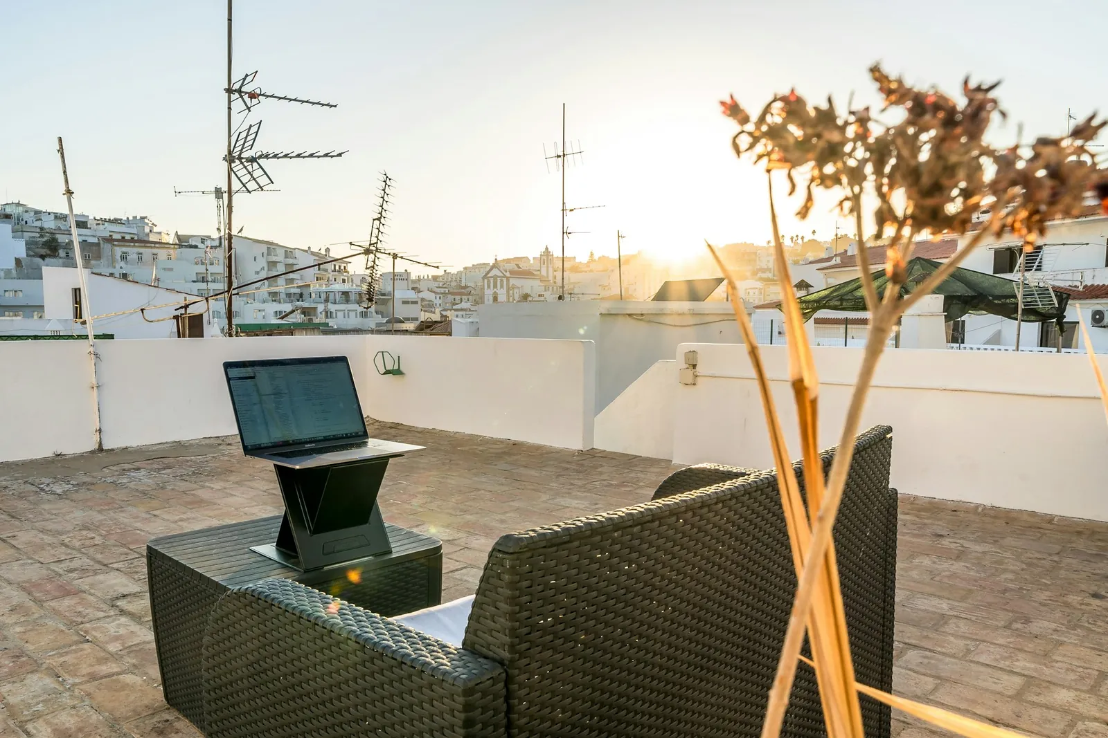 Laptop on a sunny rooftop terrace with a view of a white town at sunset