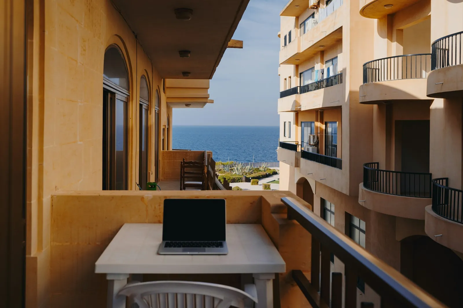Laptop on a table on a sunny balcony with a view over the blue sea