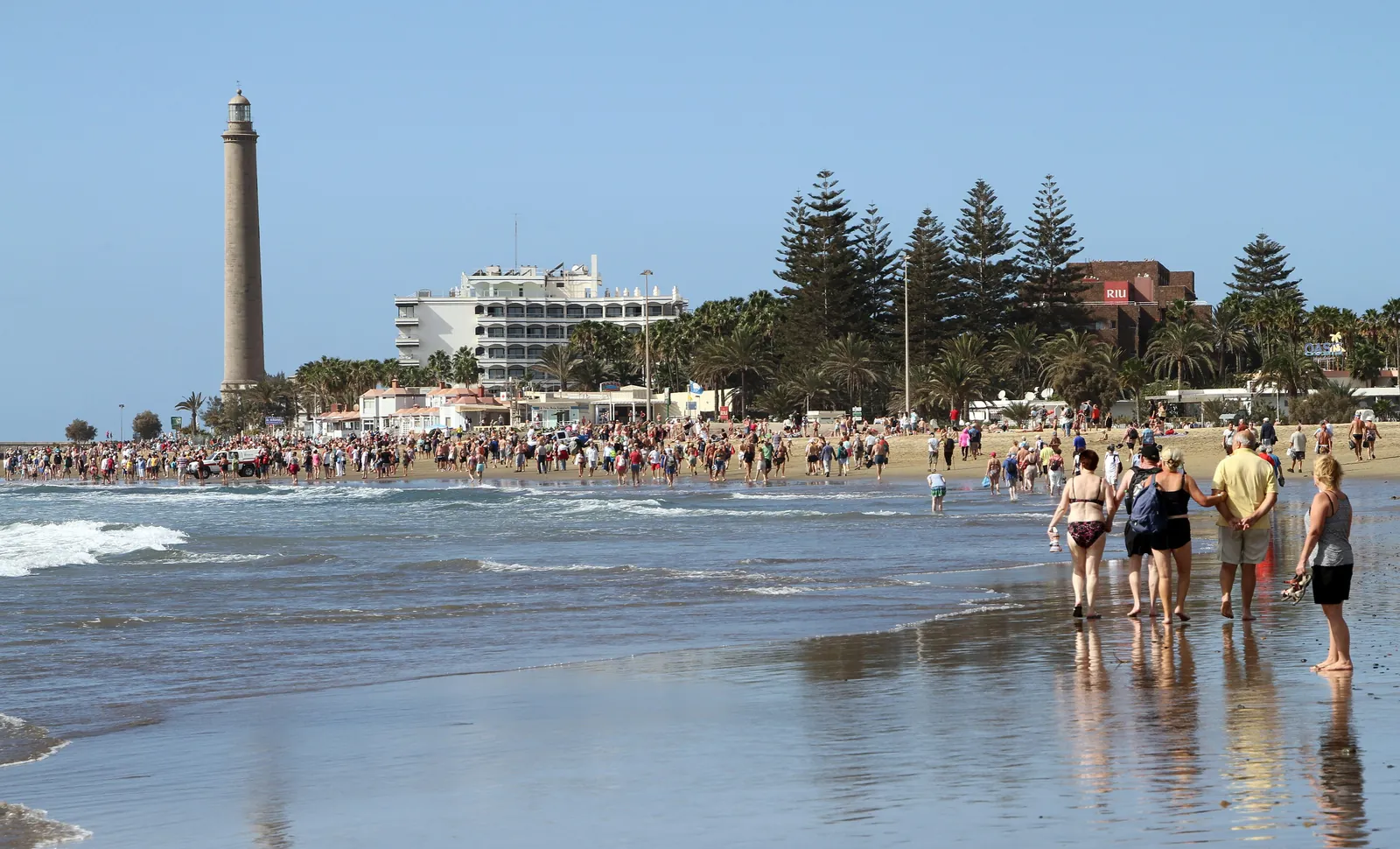 Walkers on the beach at Maspalomas with the lighthouse and palm trees along the shore