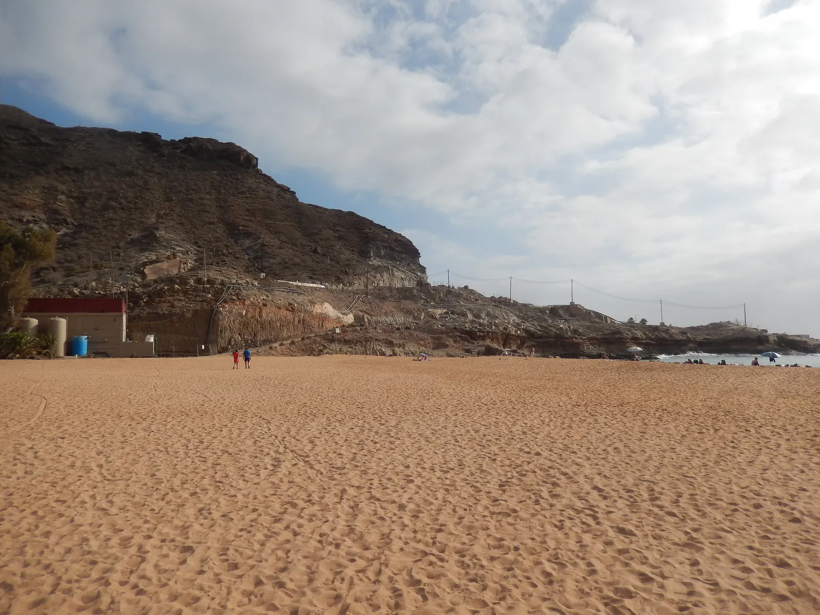 Wide sandy beach at Playa de Tauro with a brown rocky hillside rising behind it