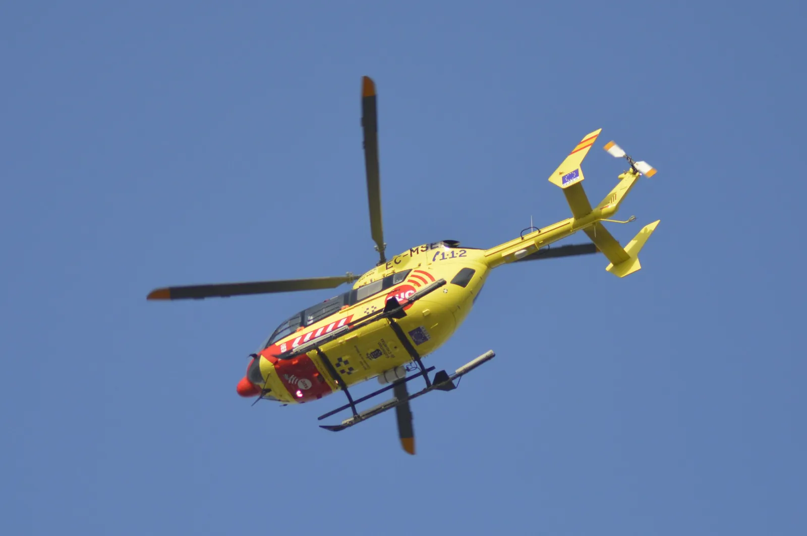 Yellow Canary emergency service helicopter marked 112 flying against a clear blue sky over Gran Canaria