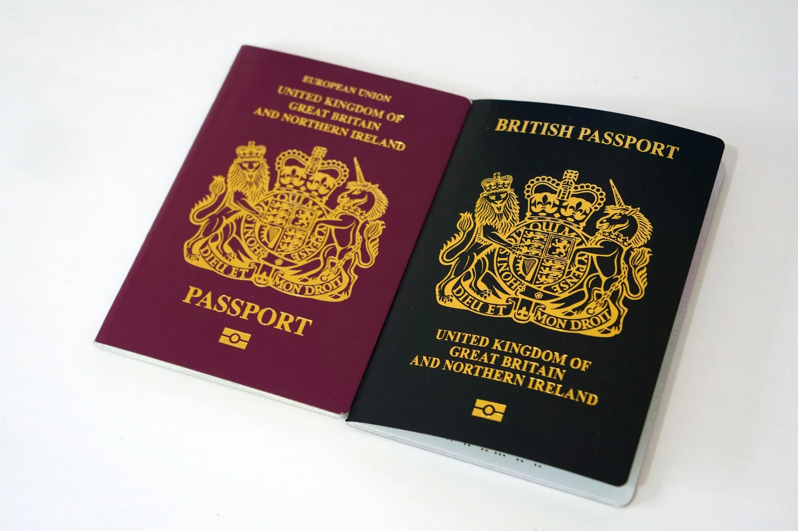 Two British passports, one burgundy and one dark blue, lying open side by side on a white table
