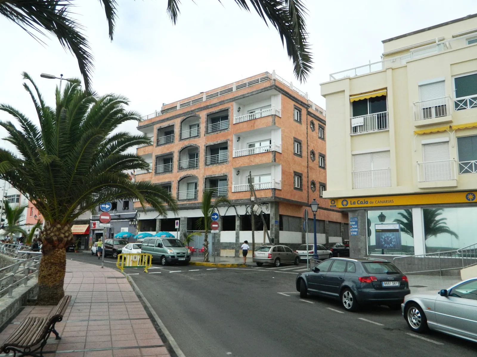 Palm-lined seafront street with parked cars and apartment buildings in Arguineguín