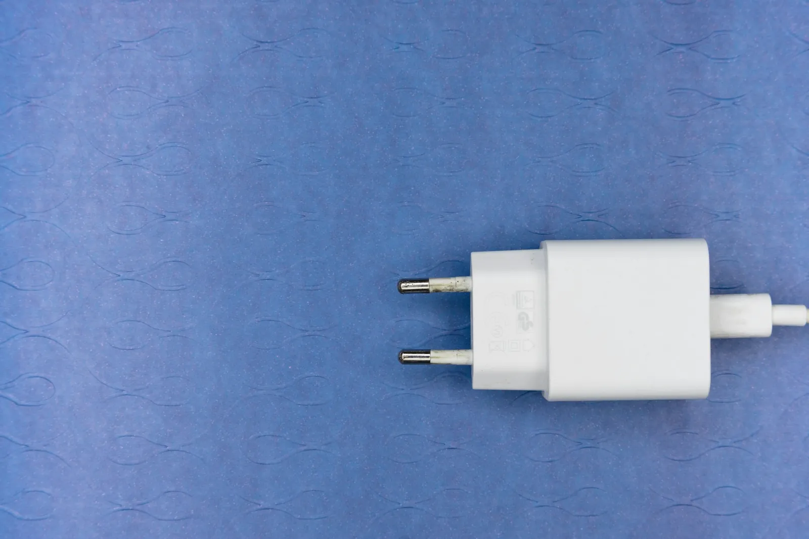 White two-pin European plug charger with round pins lying on a blue textured surface