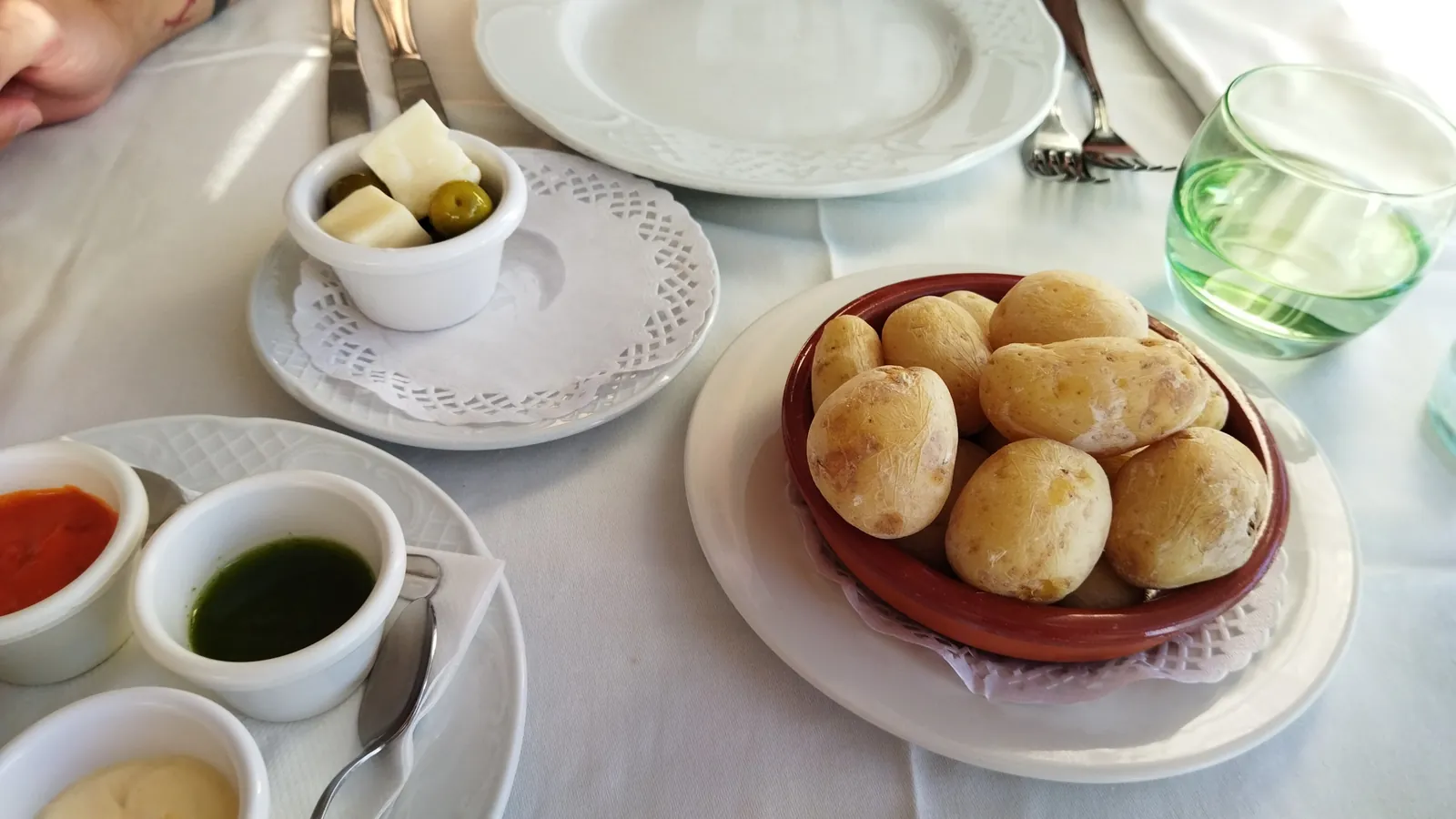 Bowl of wrinkled potatoes with red and green mojo sauces, cheese and olives on a white tablecloth