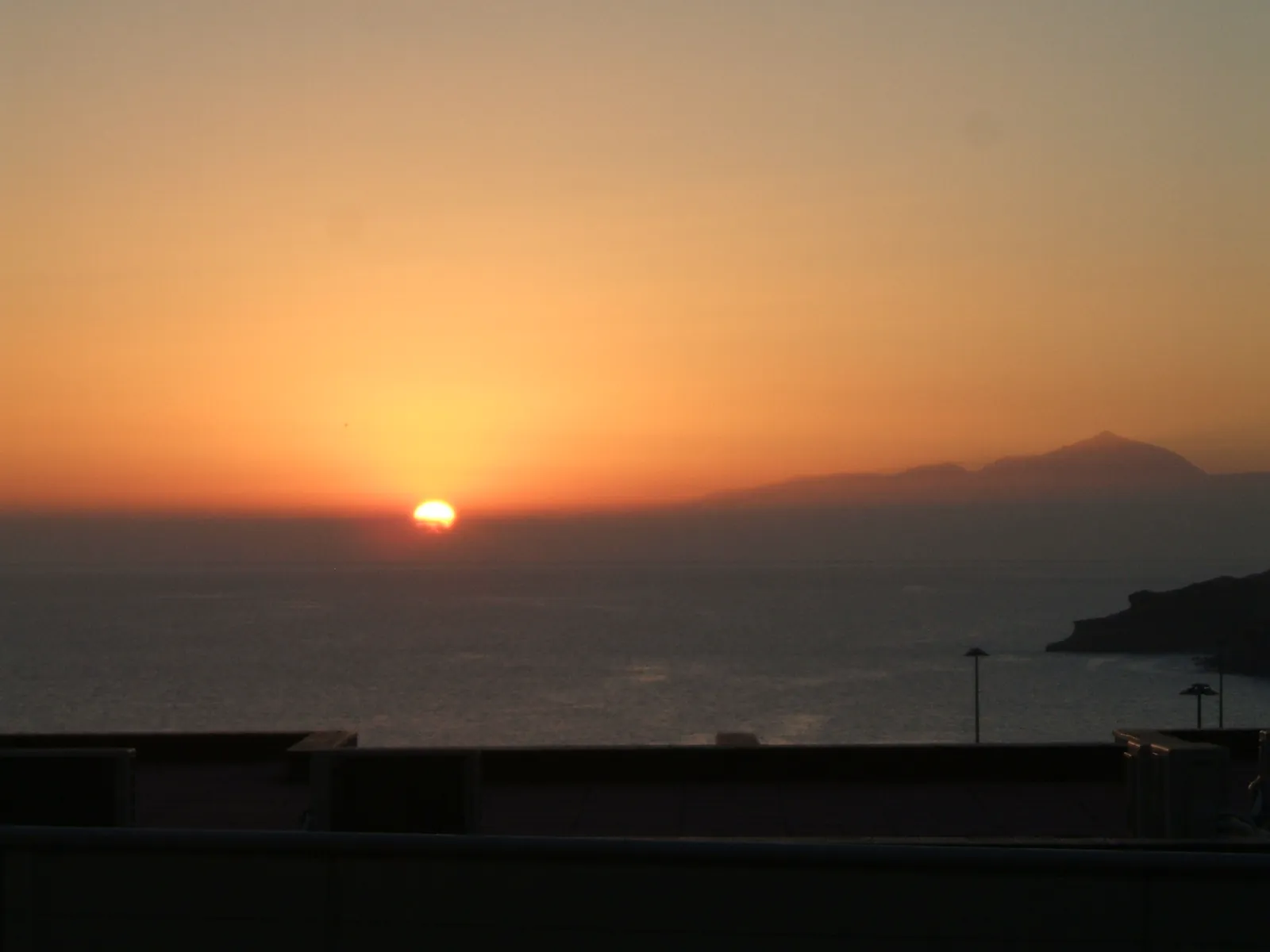 Orange sun setting over the Atlantic with Tenerife silhouetted on the horizon, seen from Arguineguín