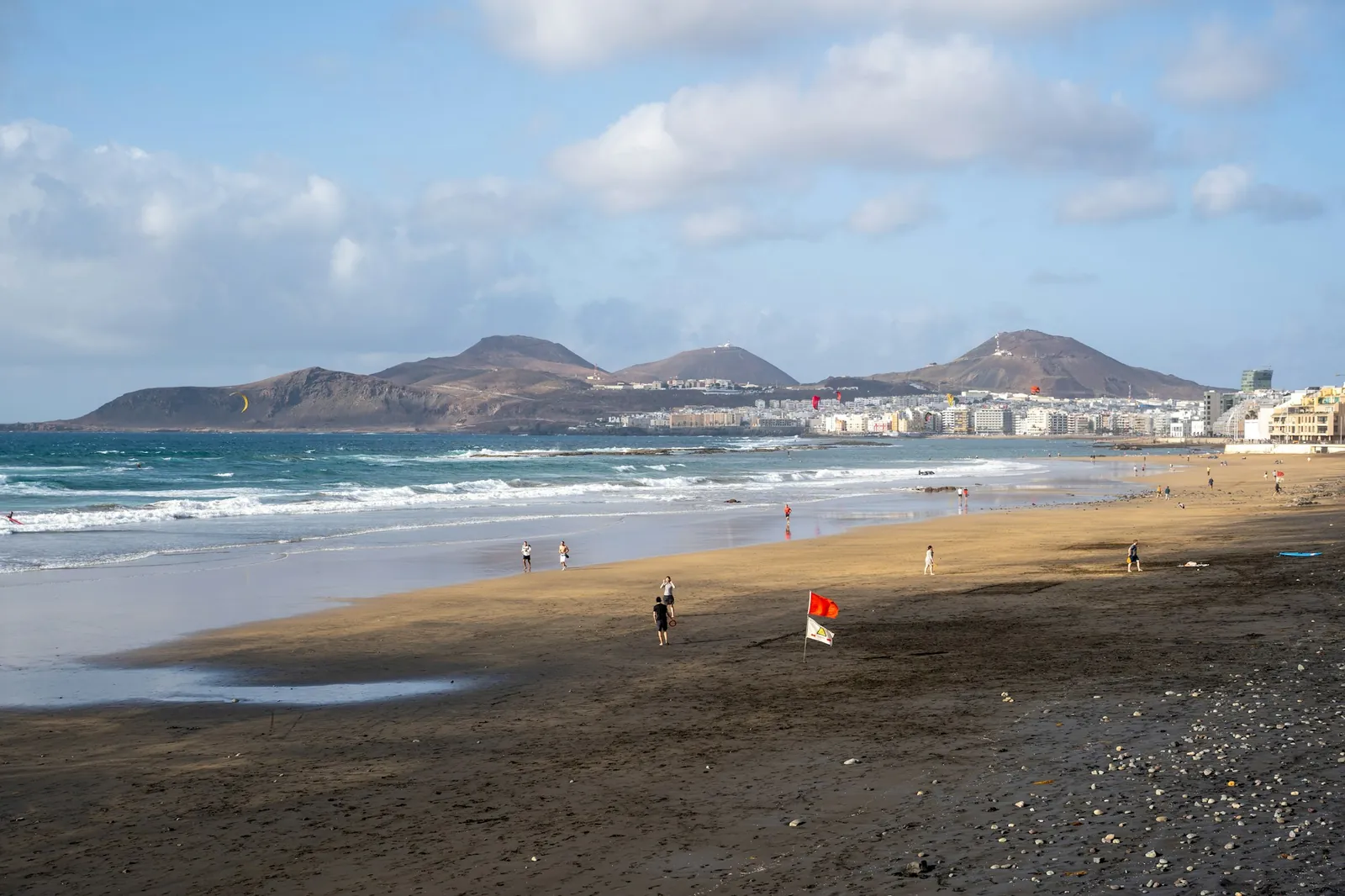 Las Canteras beach in Las Palmas with a red flag, surf and the Isleta hills in the distance