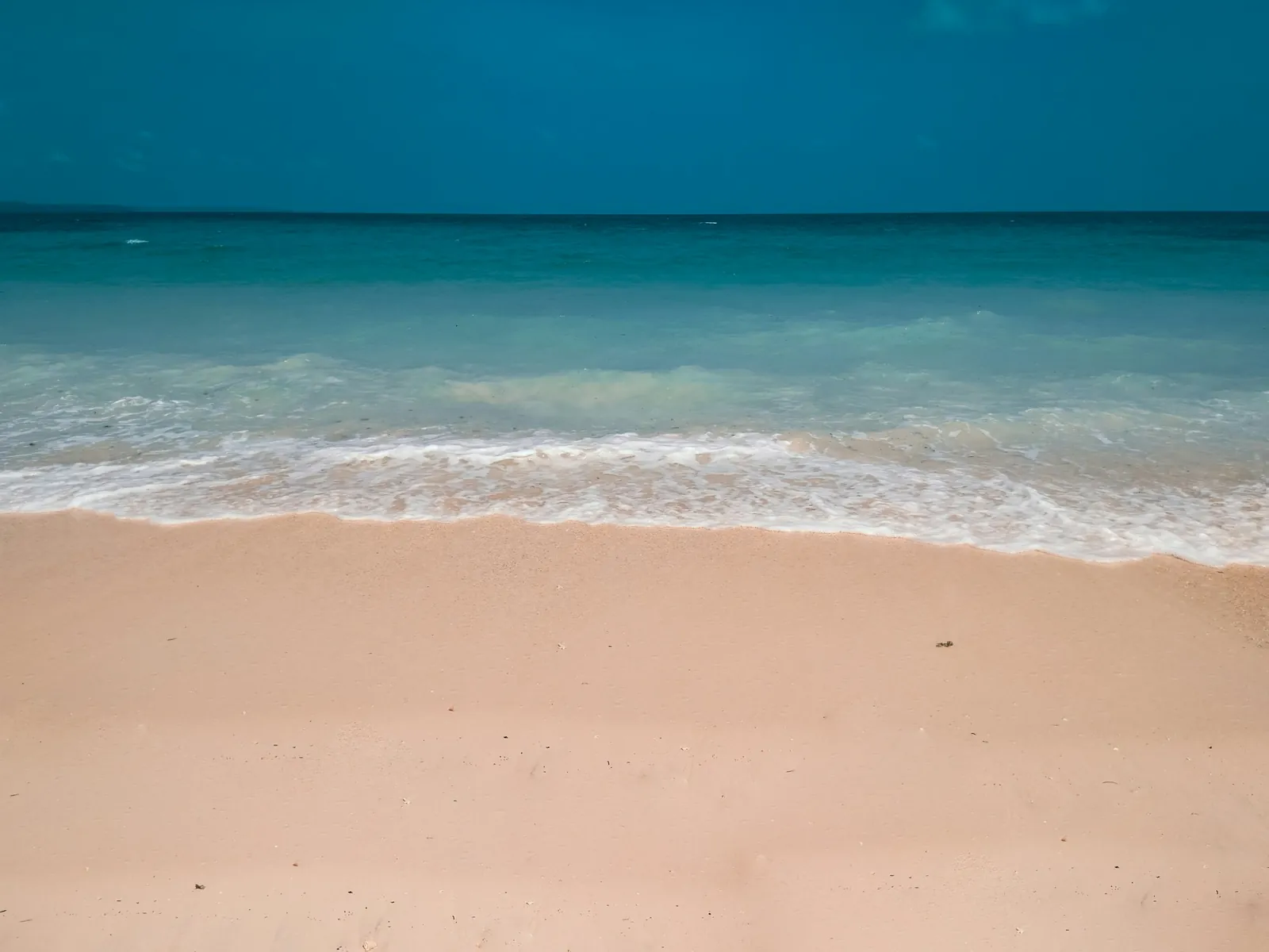 Turquoise waves washing onto a calm sandy beach under a deep blue sky