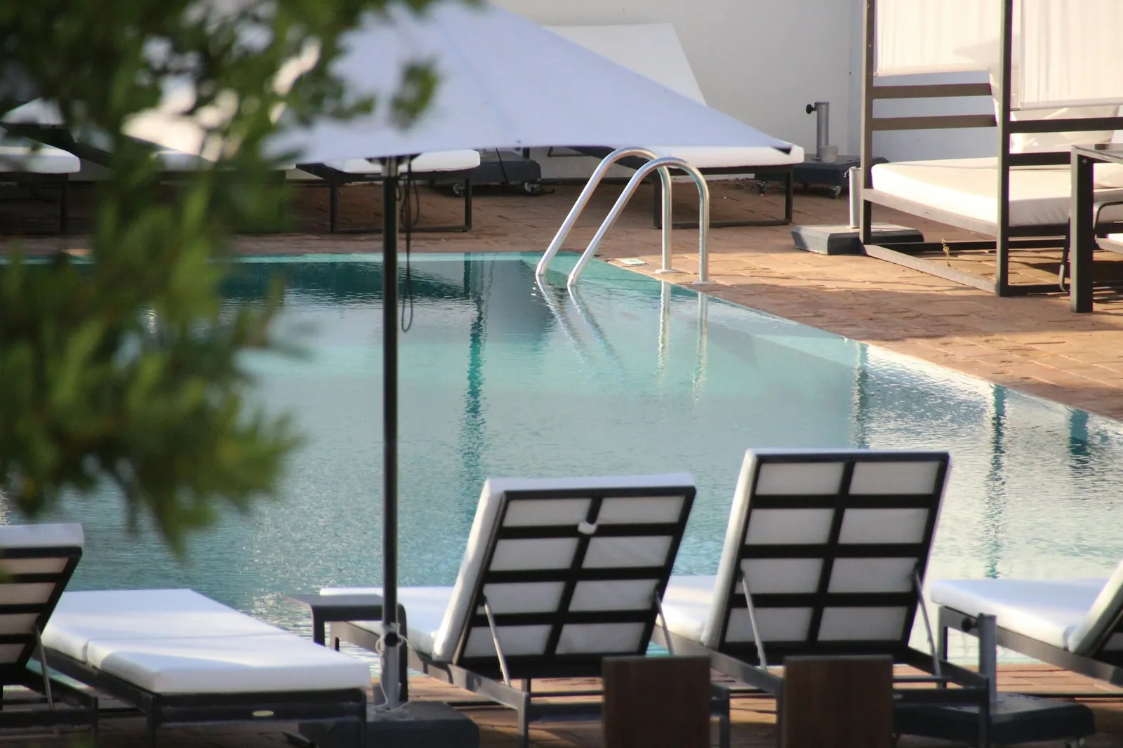 Quiet hotel pool with white sun loungers and a parasol in soft evening light