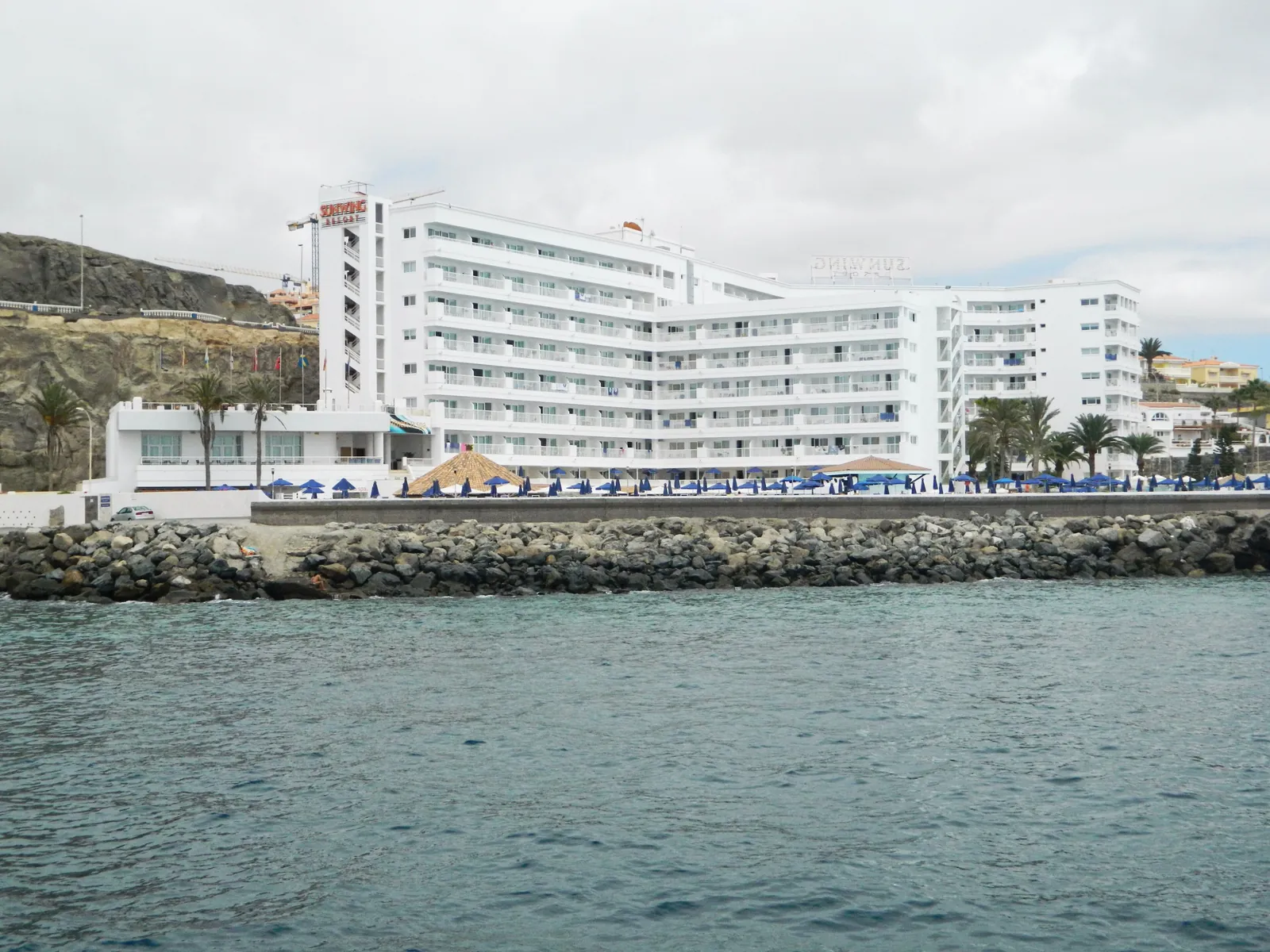 White seafront hotel with sun umbrellas beside the rocky shore at Arguineguín, seen from the sea